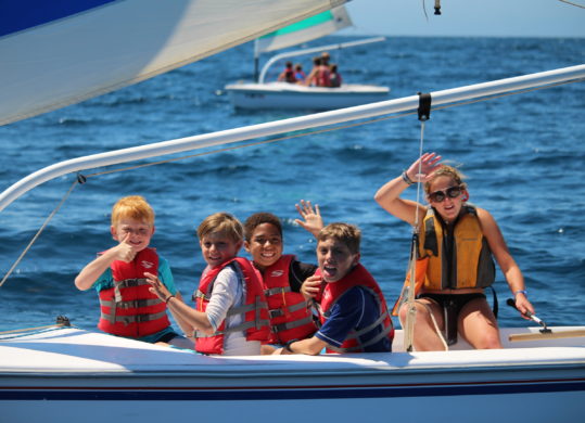 summer campers on sailboat waving