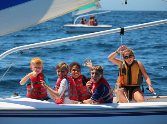 summer campers on sailboat waving