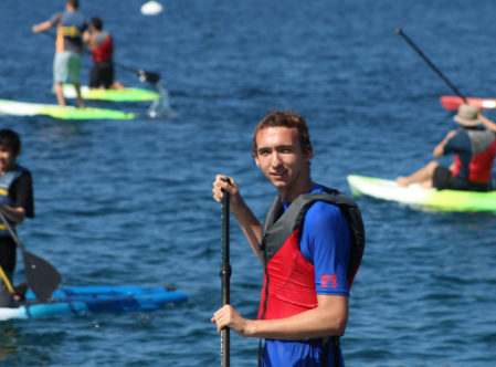 camper looking at the camera while stand up paddleboarding and other campers in the background