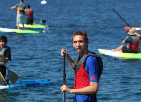camper looking at the camera while stand up paddleboarding and other campers in the background