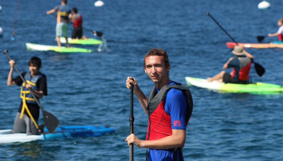 camper looking at the camera while stand up paddleboarding and other campers in the background