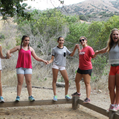 girls attempting to balance on a balance beam and form a human chain by holding hands