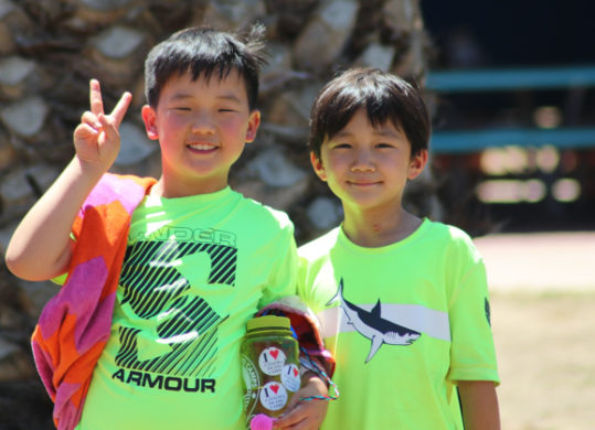 two campers smiling for a photo in green shirts with their towels and water bottles