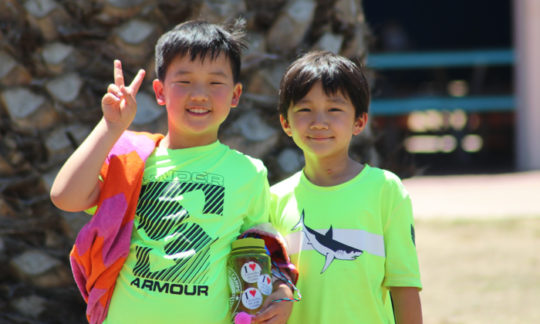 two campers smiling for a photo in green shirts with their towels and water bottles