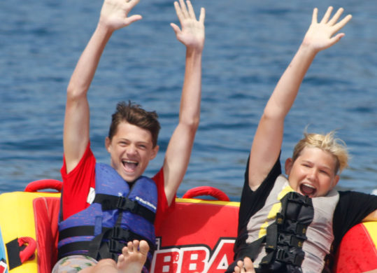 campers seated on a tube being pulled by a boat