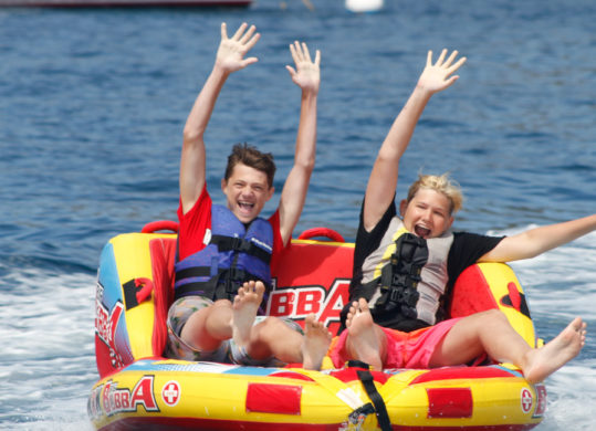 campers seated on a tube being pulled by a boat