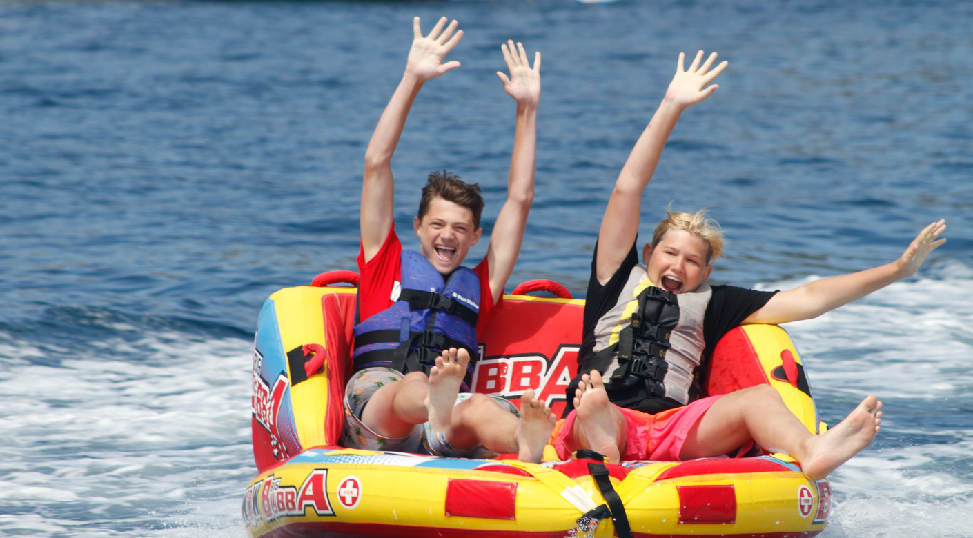 campers seated on a tube being pulled by a boat