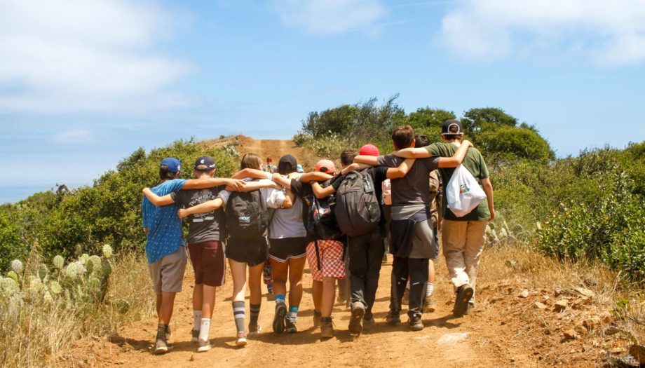 group walking up a hiking trail with arms around each other